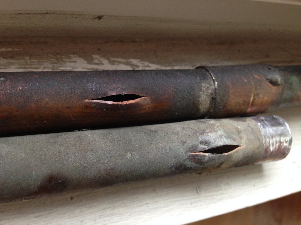 Two supply pipes split open lengthwise by a freeze, copper and galvanized, showing the classic pressure-burst seam