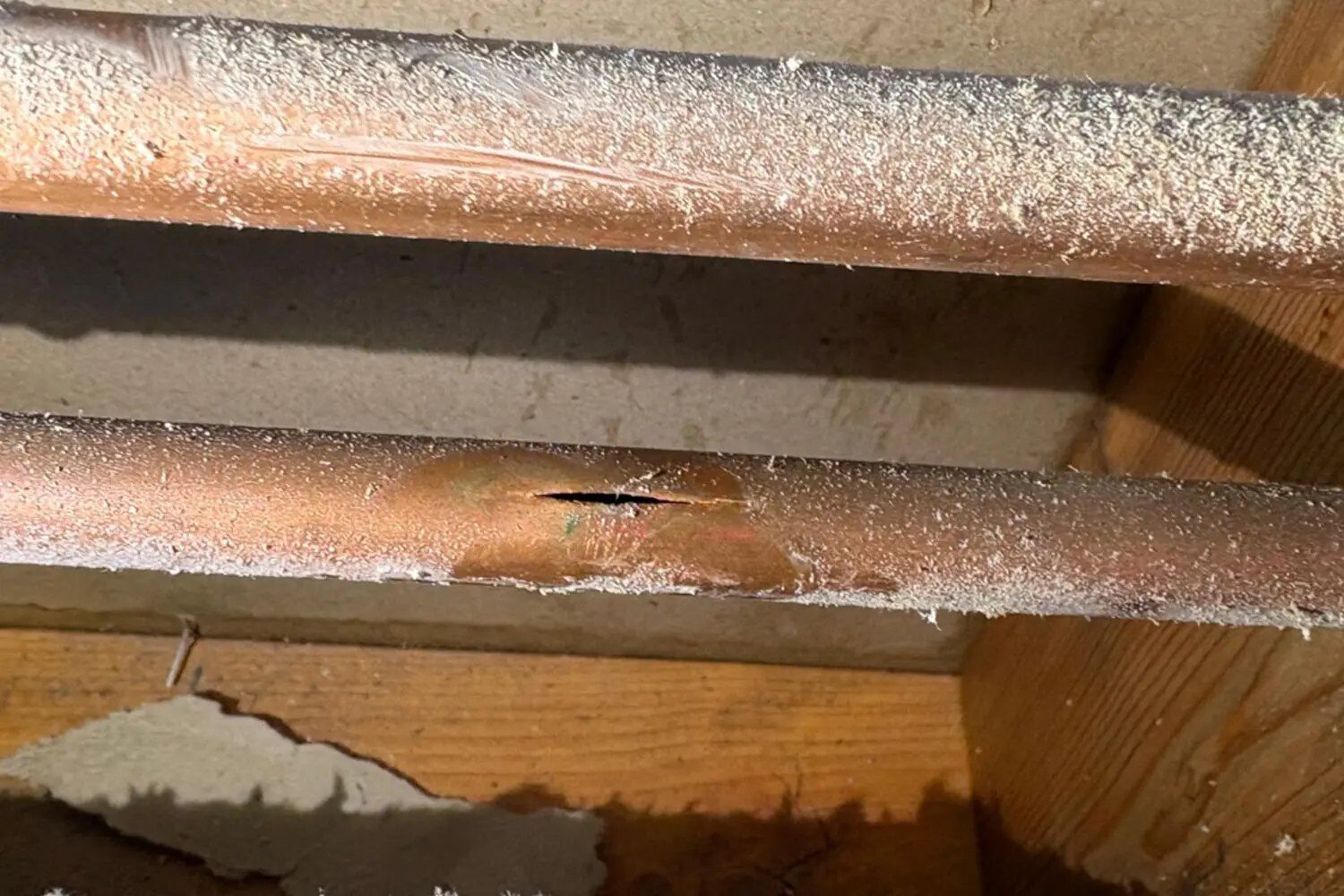 Split in a frozen copper supply line in a Michigan floor joist bay, frost still on the pipe