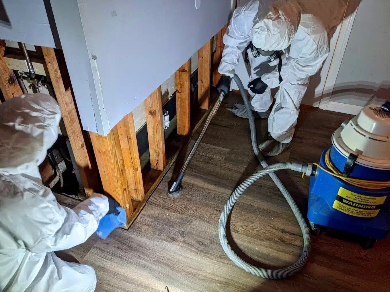 Two DriForce technicians in full hazmat suits and respirators HEPA-vacuuming and decontaminating exposed wall studs during hazardous materials cleanup in Metro Detroit