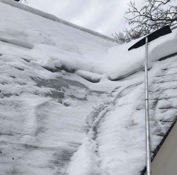 Ice dam and snow built up along the eave of a Michigan roof, cleared with a roof rake