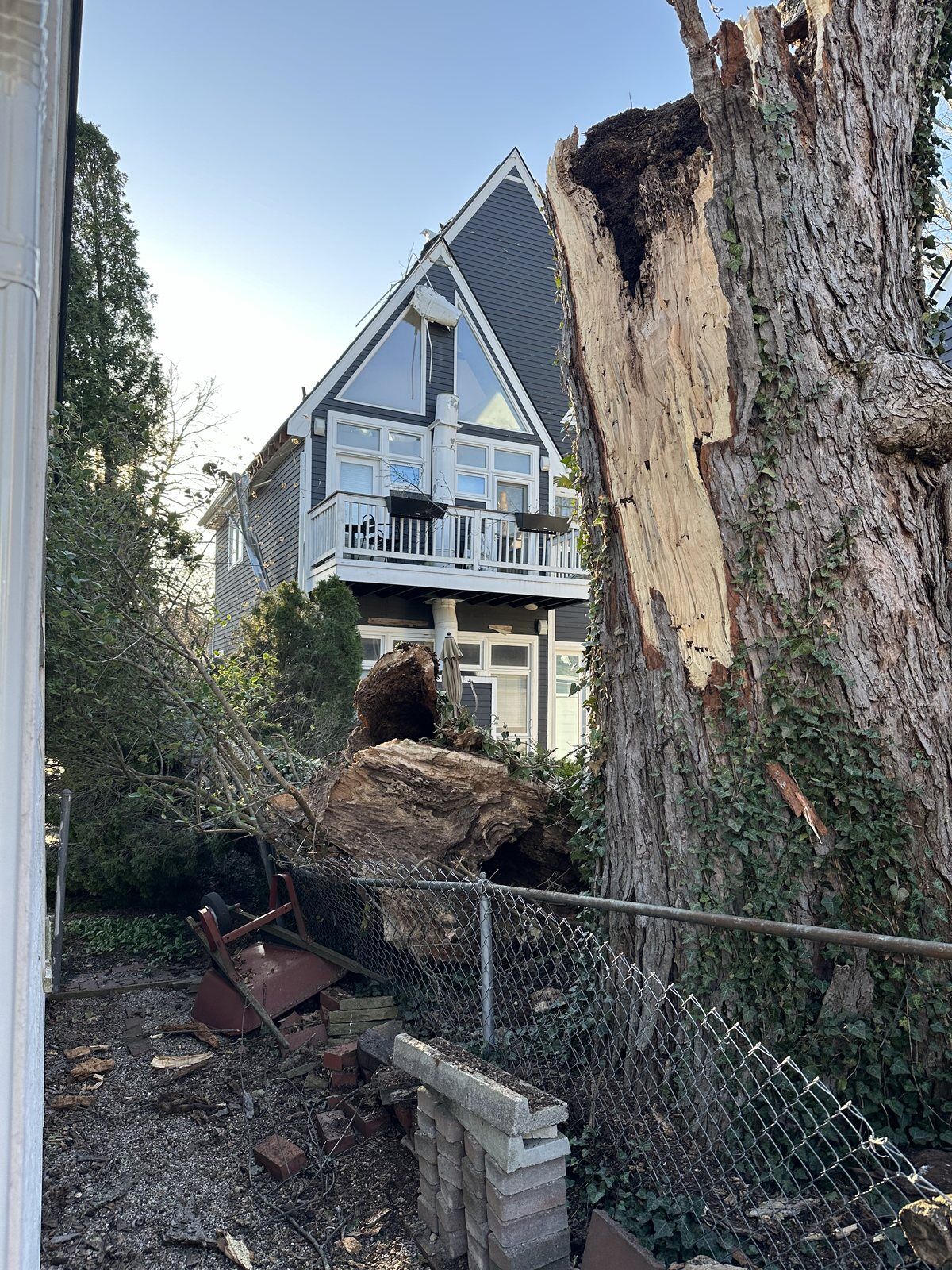 Storm-snapped tree trunk and debris beside a damaged Michigan home awaiting DriForce tree removal and structural repair